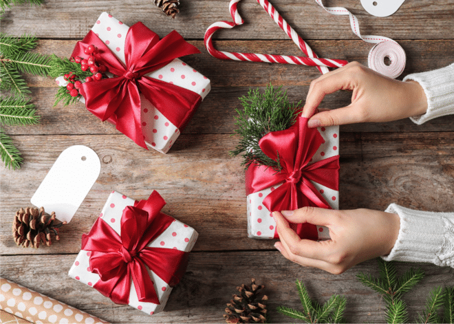 Frauenhände, die ein Geschenk mit weiß-rot gepunktetem Geschenkpapier und einer roten Schleife auf einer Holzoberfläche einwickeln