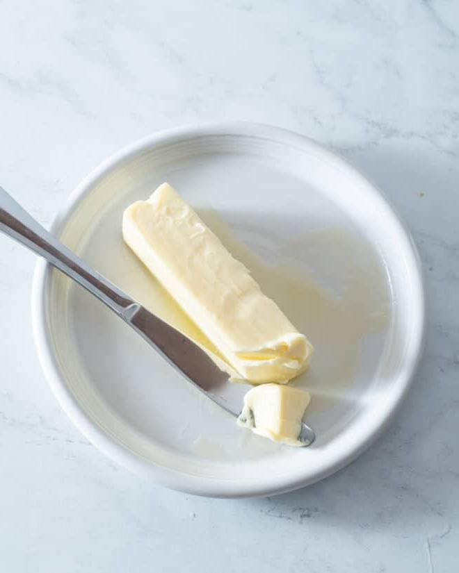 Ein Stück weiche Butter auf einem kleinen weißen Teller mit einem Buttermesser daneben