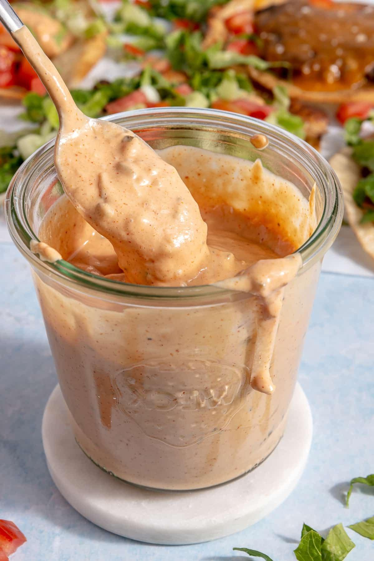 Ein Glas Burgersauce, aus dem jemand mit einem Löffel etwas Sauce schöpft.
