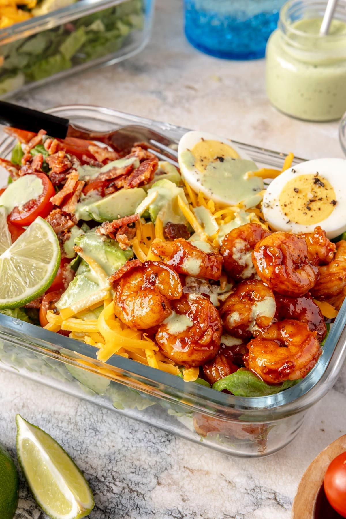 Ein Glas-Meal-Prep-Behälter gefüllt mit scharfem Garnelen-Cobb-Salat.