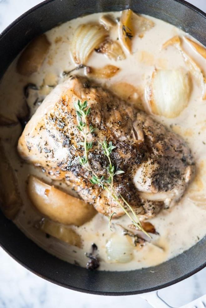 Saftiger Schweinefiletbraten mit Apfelwein, umgeben von Äpfeln und Zwiebeln, auf einem Backblech angerichtet.