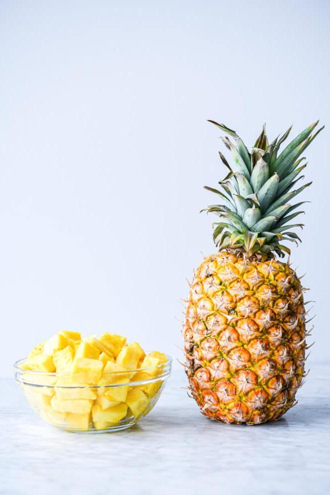 Eine ganze, ungeschnittene Ananas neben einer Schale mit gewürfelten, frischen Ananasstücken