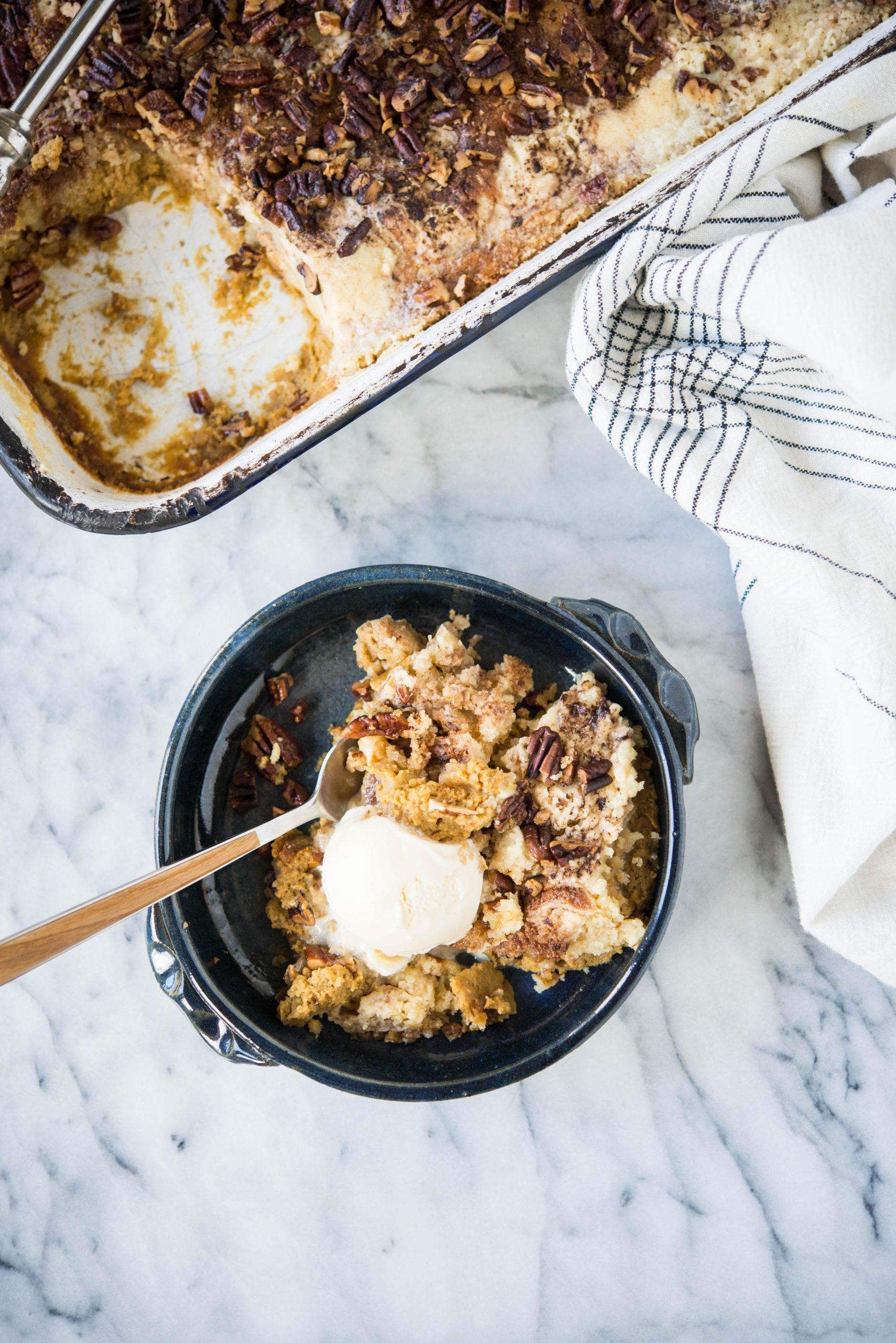 Dunkelblaue Schüssel mit Kürbis-Dump-Cake und einer Kugel Eiscreme darauf.