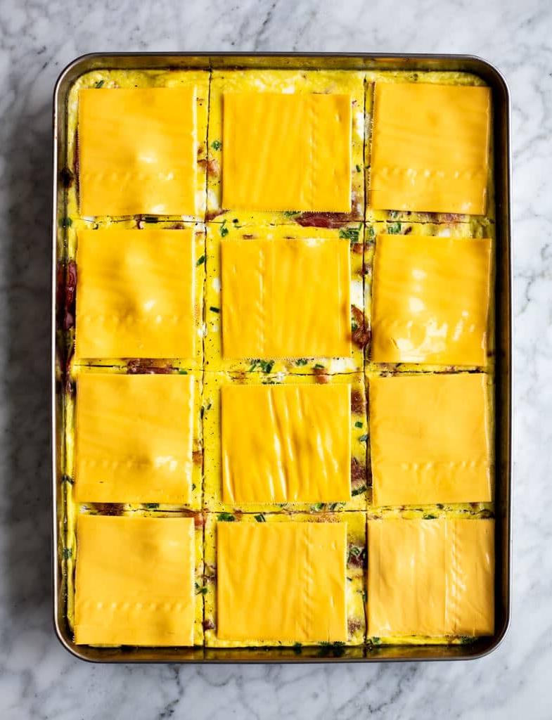 Backblech mit Speck, gebackenen Eiern und Schnittlauch, in Quadrate geschnitten und mit Käsescheiben belegt.