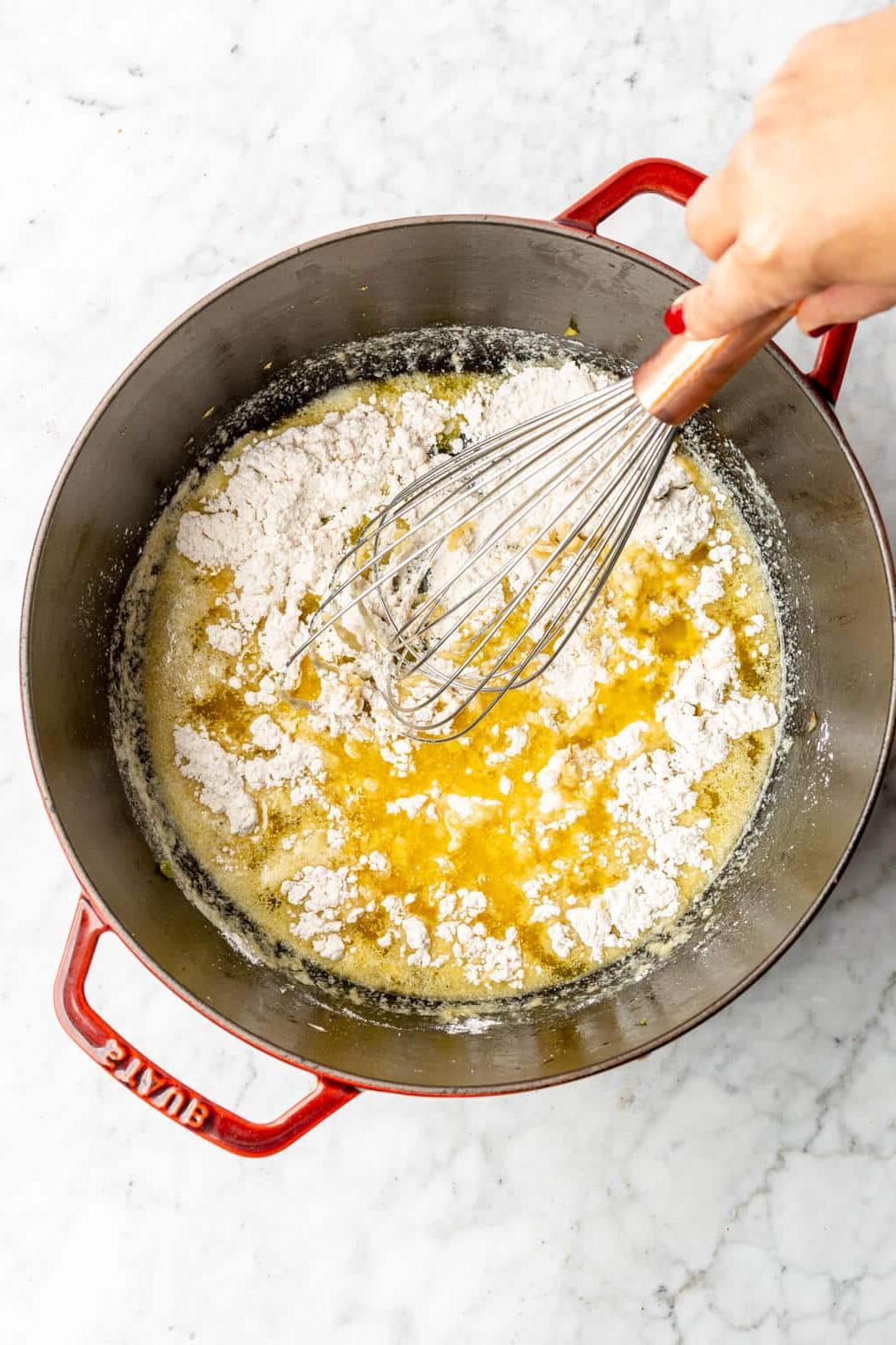 Hand rührt geschmolzene Butter und Mehl zusammen in einem großen holländischen Ofen.