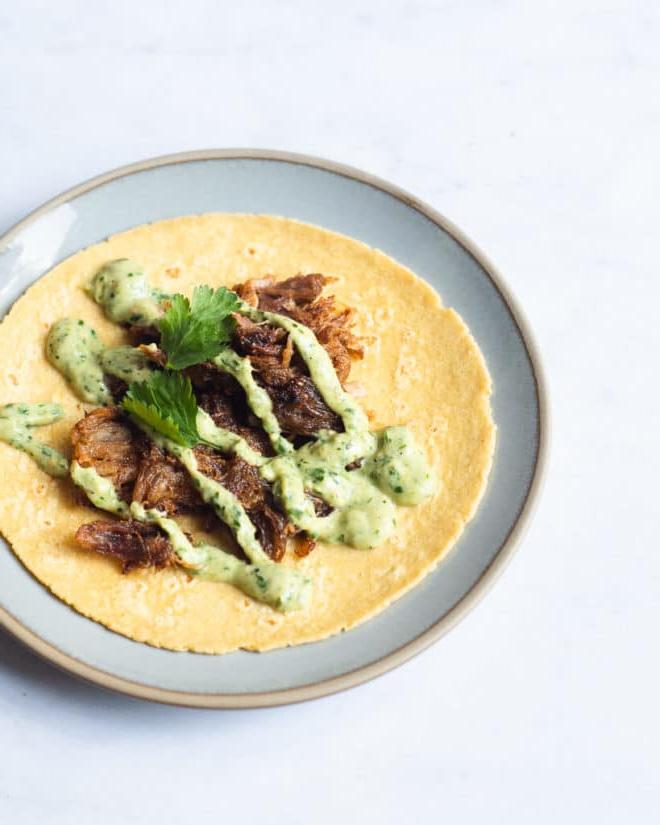 Instant Pot Carnitas Tacos 5 Ein einzelner Carnitas Taco, belegt mit cremiger Avocado-Verde-Sauce und Koriander, offen auf einem kleinen blauen Teller
