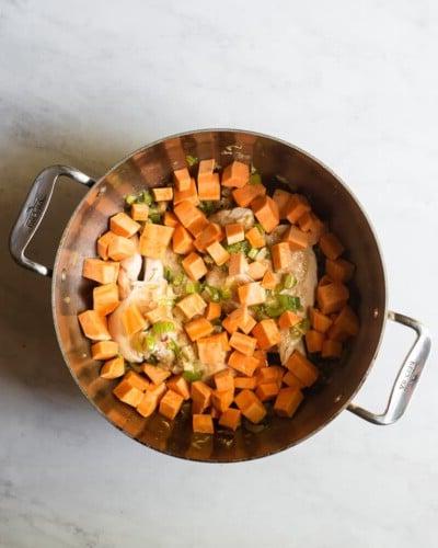 Ein großer Edelstahltopf mit Hähnchen, gewürfelten Süßkartoffeln und Sellerie