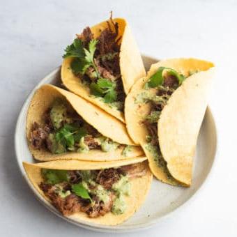 Instant Pot Carnitas Tacos 6 Ein Teller mit 4 Carnitas Tacos, belegt mit cremiger Avocado-Verde-Sauce und Koriander