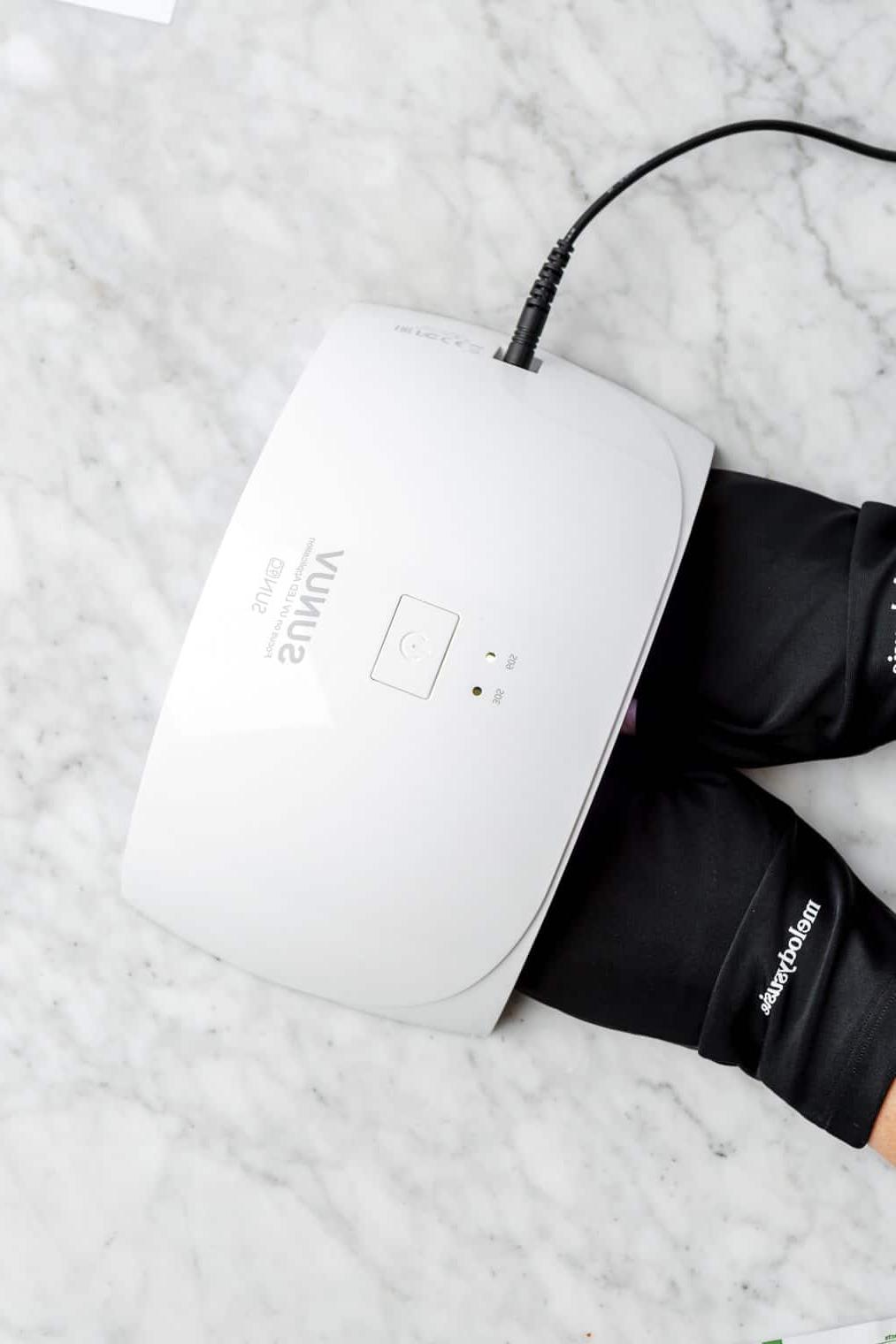 Hände tragen schwarze Handschuhe und härten unter einer UV-Lampe aus.