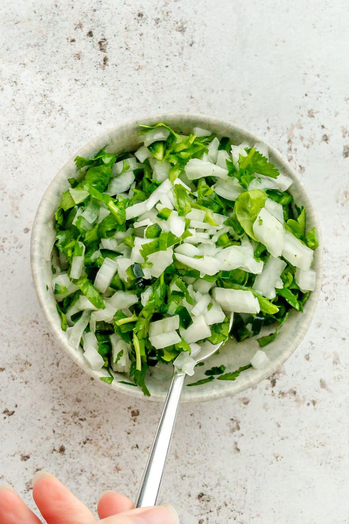 Eine Zwiebel-Koriander-Jalapeño-Salsa wird in einer kleinen blauen Keramikschüssel auf hellem Hintergrund umgerührt.