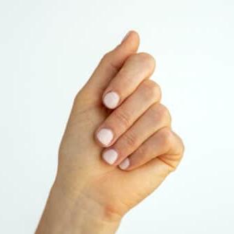 Hand mit lackierten, hellrosa Nägeln vor weißem Hintergrund.