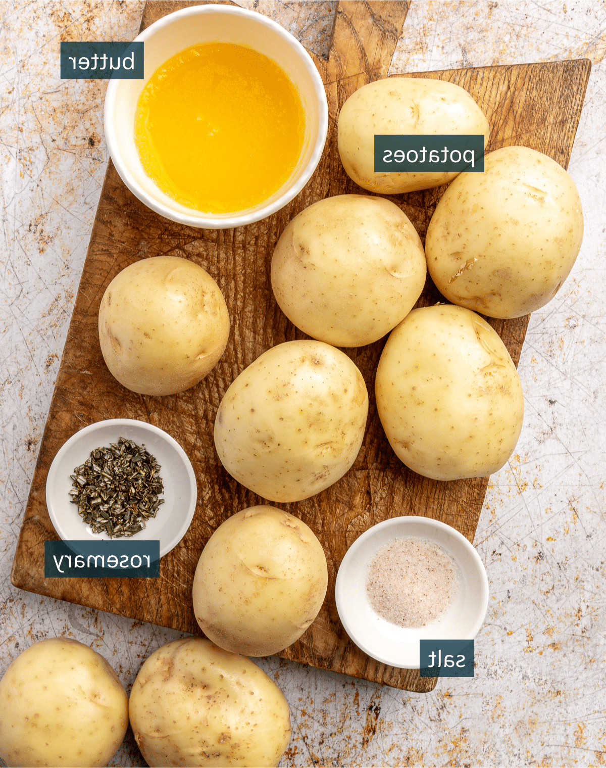 Zutaten für Rosmarin Hasselback Kartoffeln liegen in verschiedenen Schalen und auf einem Holzschneidebrett bereit.