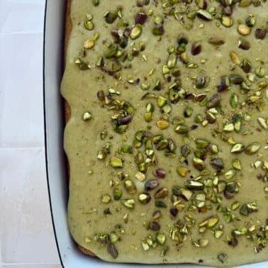 Nahaufnahme eines Stücks Pistazienkuchen mit üppiger Hüttenkäse-Glasur und gehackten Pistazien darauf.