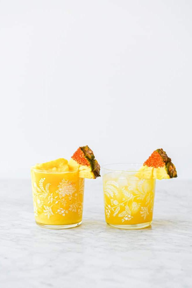 Zwei Margarita-Gläser (eins mit gefrorenem Ananas Margarita und eins mit Ananas Margarita auf Eis), garniert mit einem in Chili-Salz getauchten Ananas-Keil.
