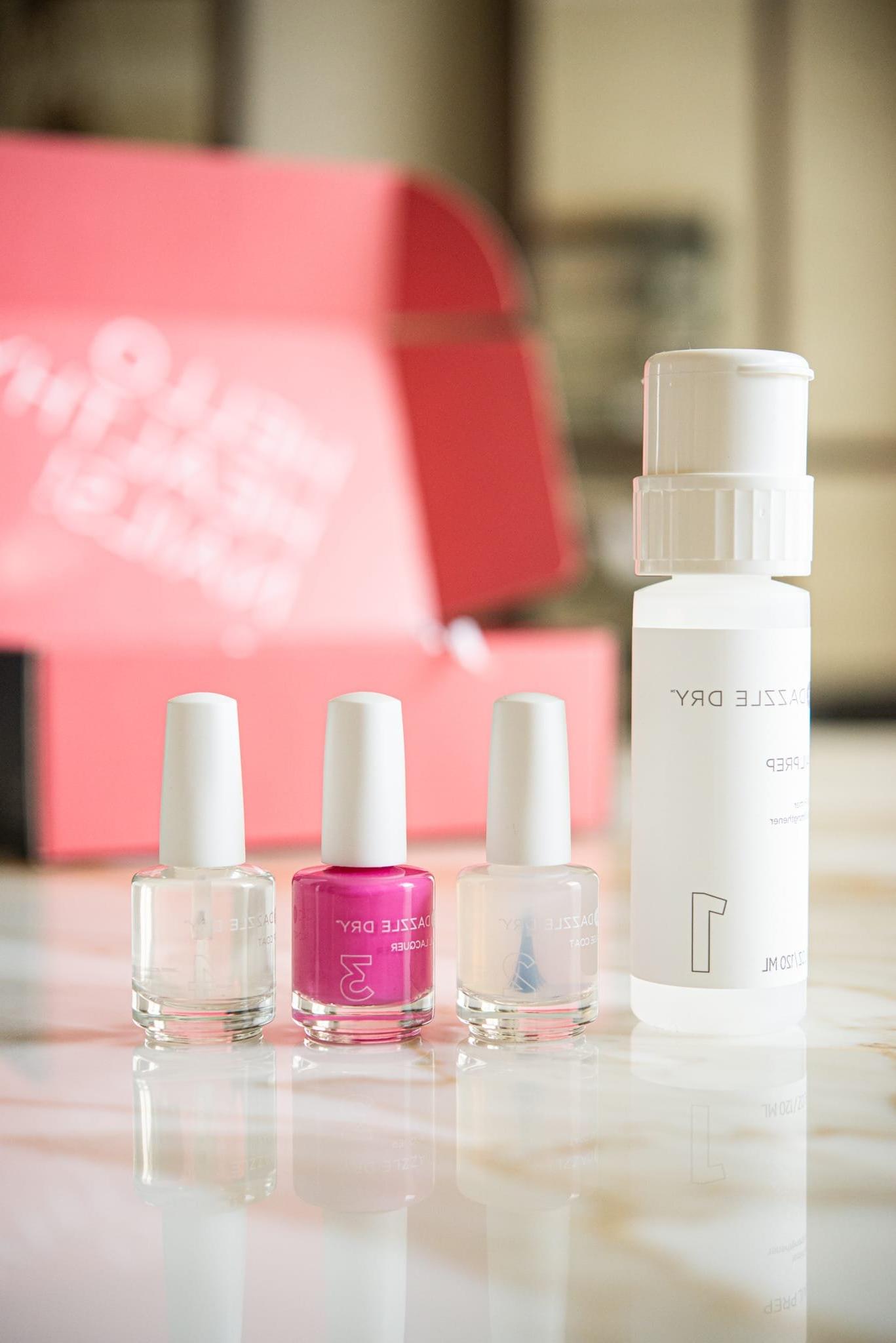 Dazzle Dry Nagelsystem – ein Arrangement aus leuchtend pinkem Nagellack neben zwei klaren Nagellacken und einem passenden Entferner, kunstvoll platziert auf einem eleganten Marmortisch.