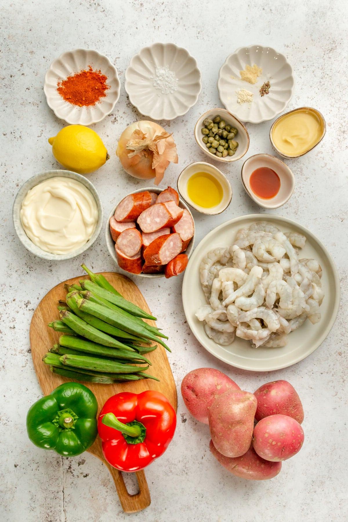 Zutaten für Cajun Garnelen-Ofenblech-Gericht in verschiedenen Schüsseln und Tellern auf hellem Untergrund arrangiert