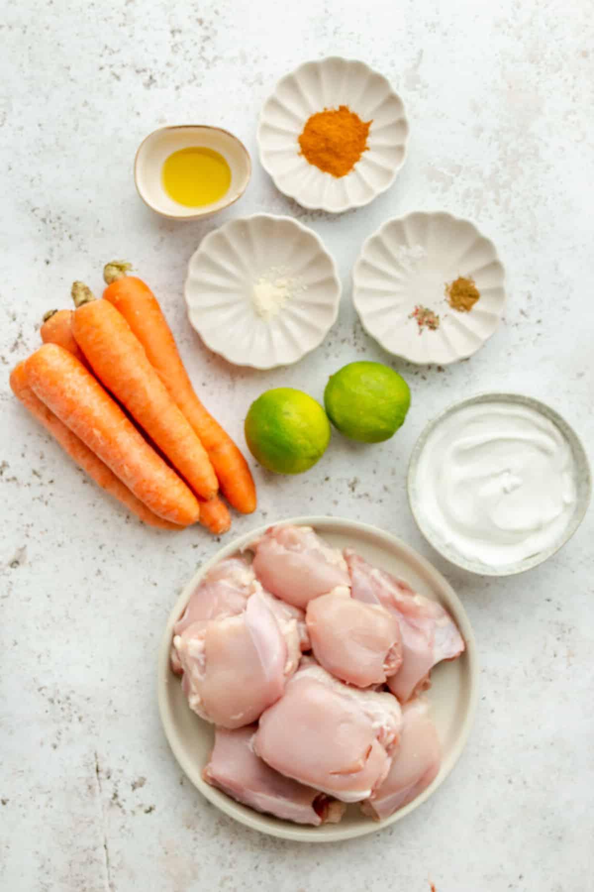 Zutaten für Blech-Curry-Hähnchenschenkel auf verschiedenen Tellern und Schalen auf hellem Untergrund.