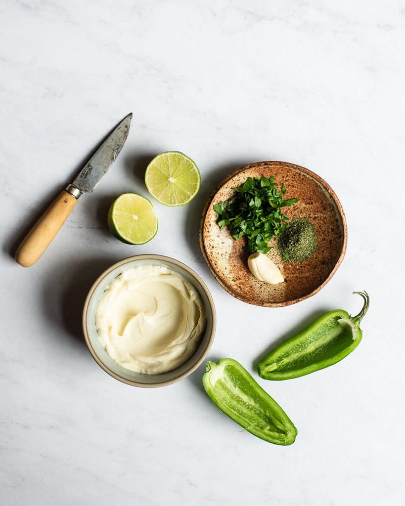 Alle Zutaten für ein selbstgemachtes Jalapeño Ranch Dressing in verschiedenen Schalen und auf Tellern auf einer Marmoroberfläche.
