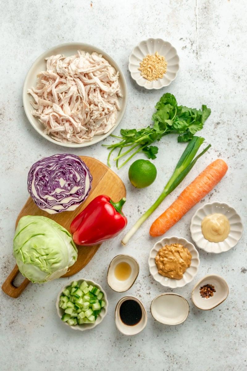 Zutaten für den Thai-inspirierten Hähnchensalat in verschiedenen Schüsseln auf einer hellgrauen Arbeitsplatte.