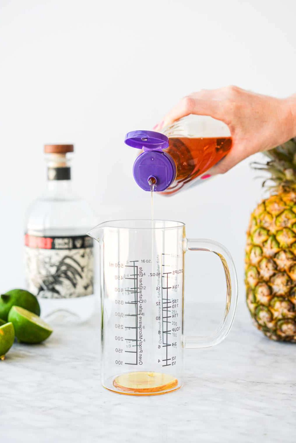 Eine Person drückt Agavendicksaft in einen großen Messbecher aus Glas.
