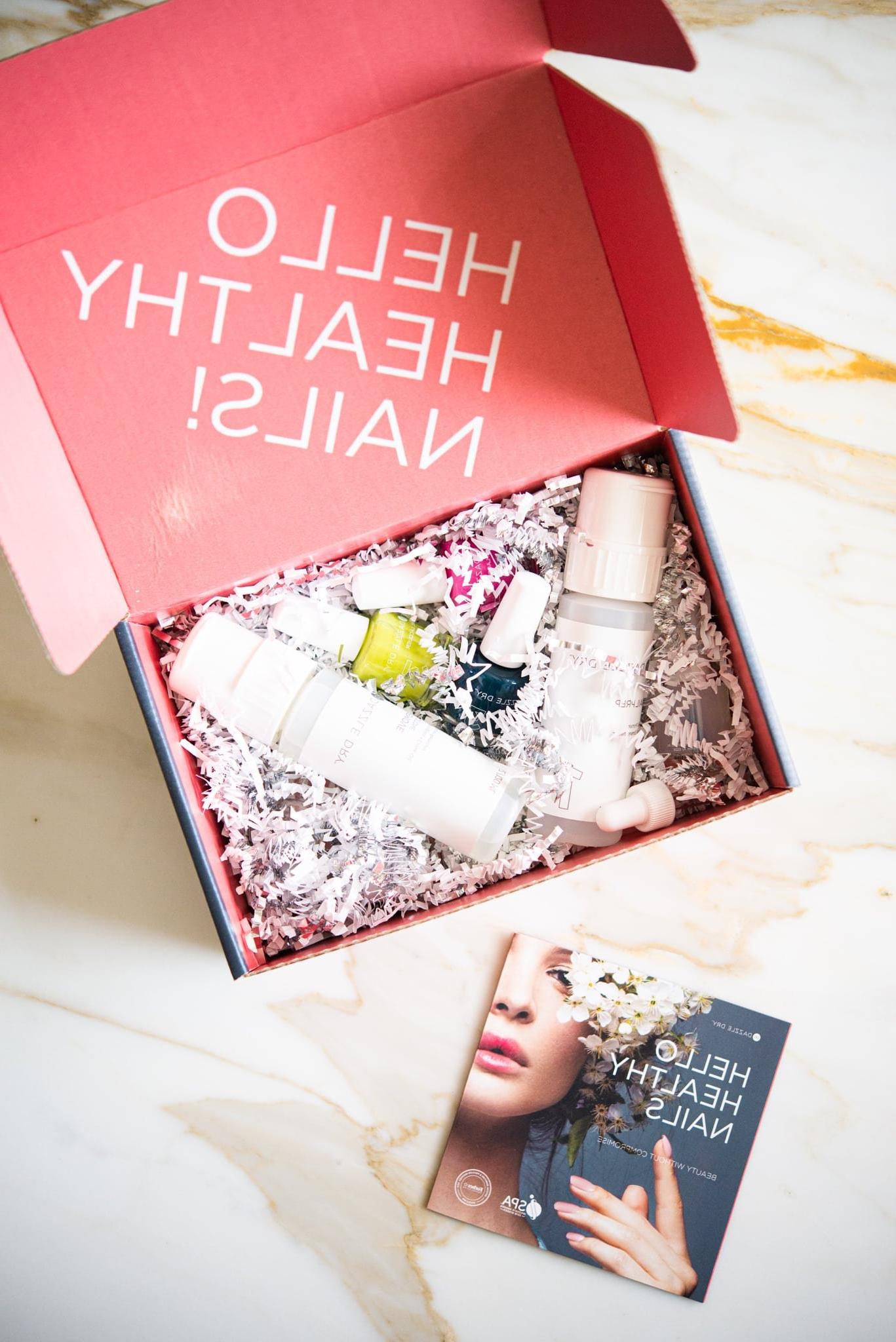 Eine rosa Box, gefüllt mit 3 verschiedenen Nagellackfarben, zwei klaren Lacken und einem Nagellackentferner, elegant platziert auf einer edlen Marmoroberfläche – das komplette Dazzle Dry System für zu Hause.