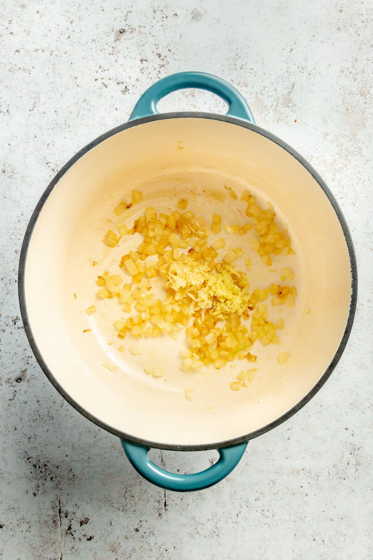 Angebratene Zwiebeln, Knoblauch und Ingwer in einem großen emaillierten Gusseisentopf.