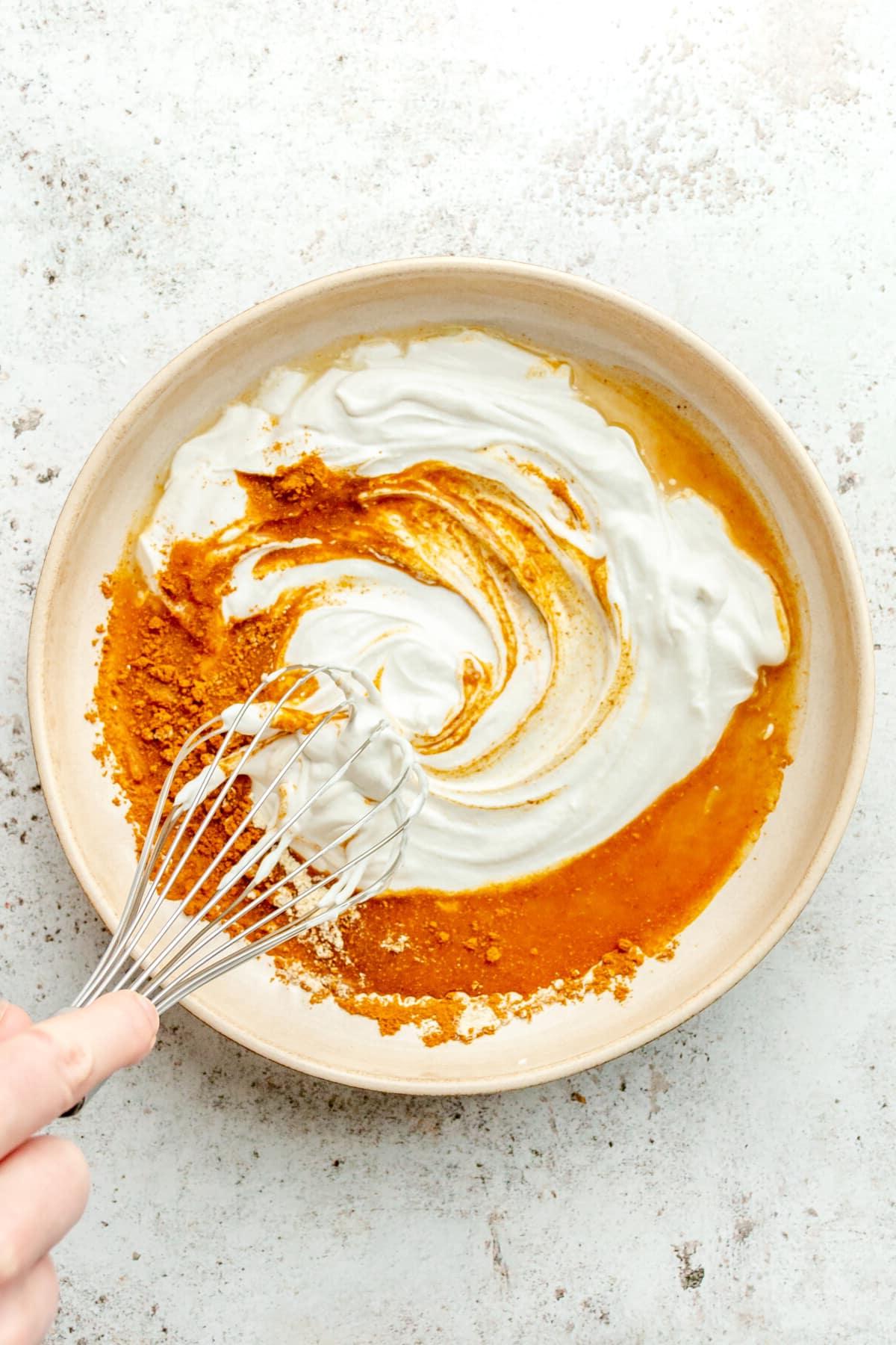 Eine Currysaucenmischung wird in einer flachen Keramikschale auf einer hellgrauen Oberfläche verquirlt.