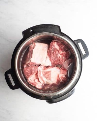 210414_Carnitas-26 Ein Instant Pot mit Wasser und Stücken von roher Schweineschulter darin