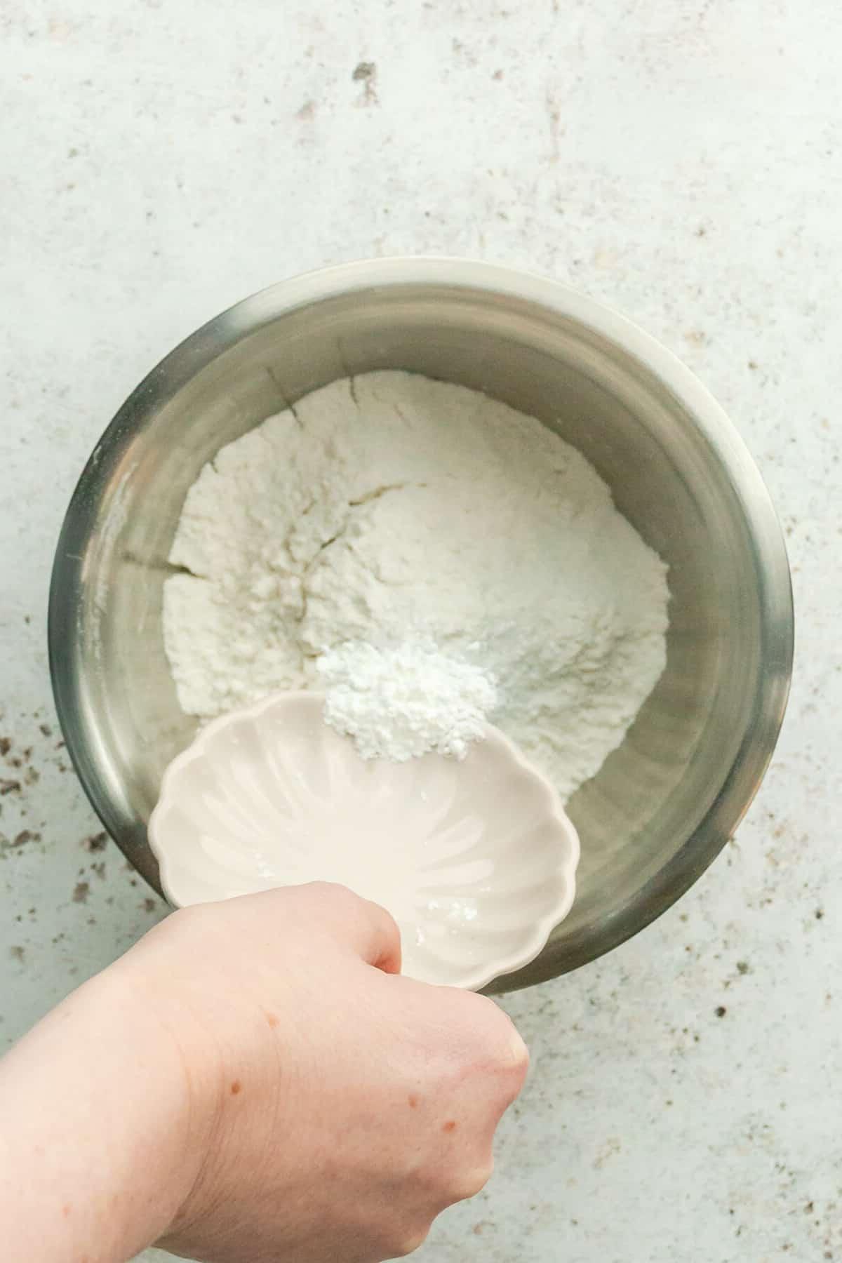 Natron wird über Mehl in einer Edelstahlschüssel auf hellem grauem Untergrund gegeben.