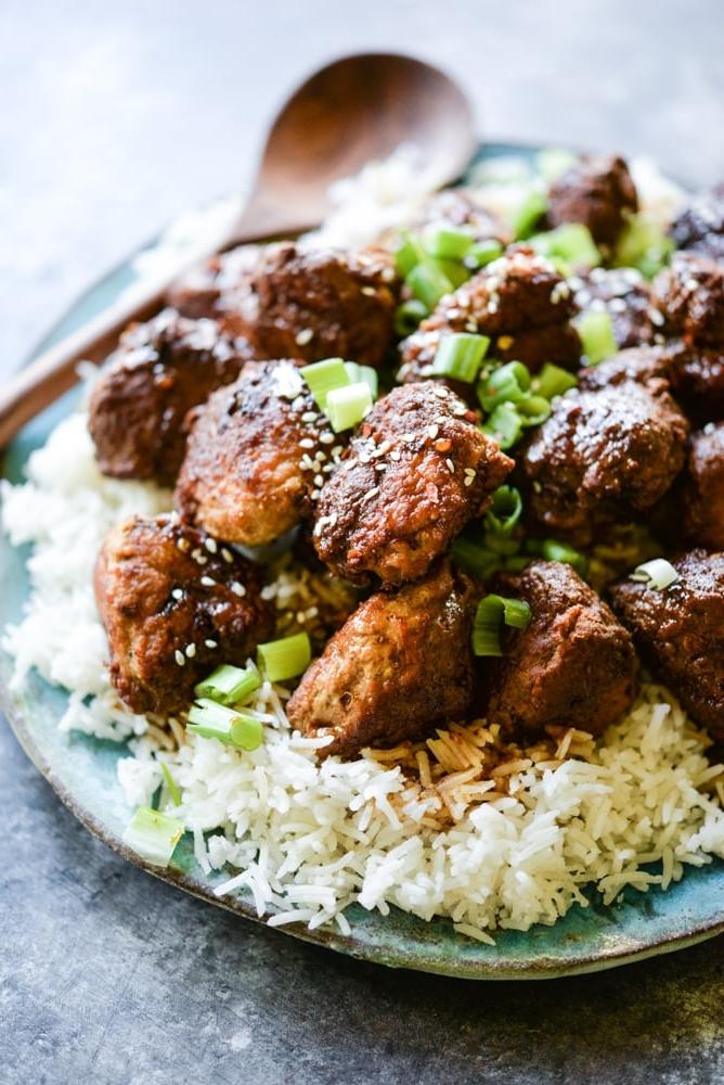 Teriyaki-Puten-Hackbällchen auf einem Bett aus Reis auf einem blauen Teller mit einem hölzernen Servierlöffel