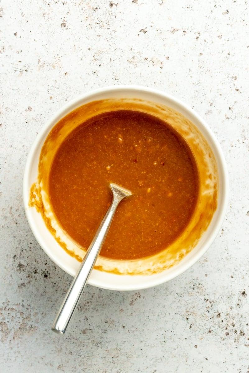 Eine orangefarbene, cremige Mischung in einer weißen Schüssel mit einem Metalllöffel.