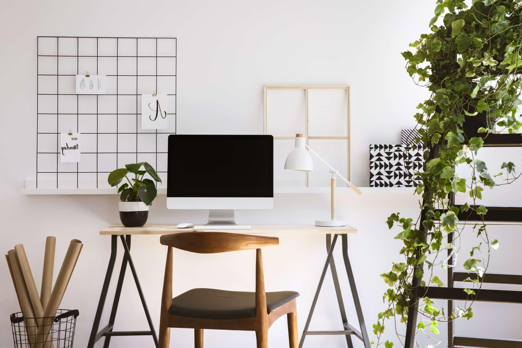 office with a white desk, mac monitor, wooden chair, and a shelf with a plant on it