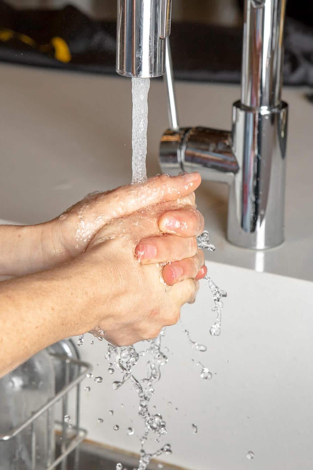 Hände werden in einem Waschbecken mit weißer Arbeitsplatte gewaschen.