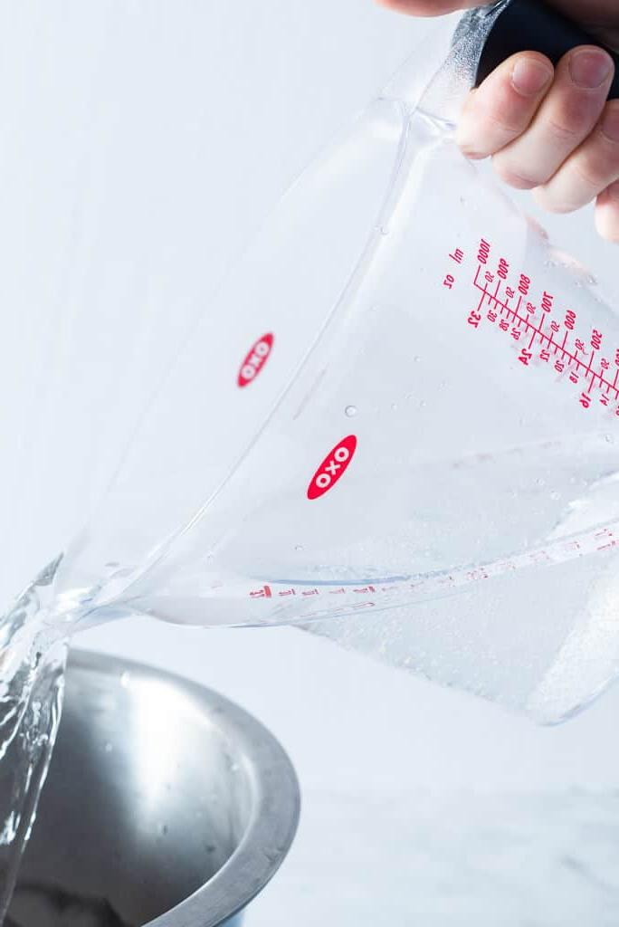 Eine Person gießt Wasser aus einem Messbecher