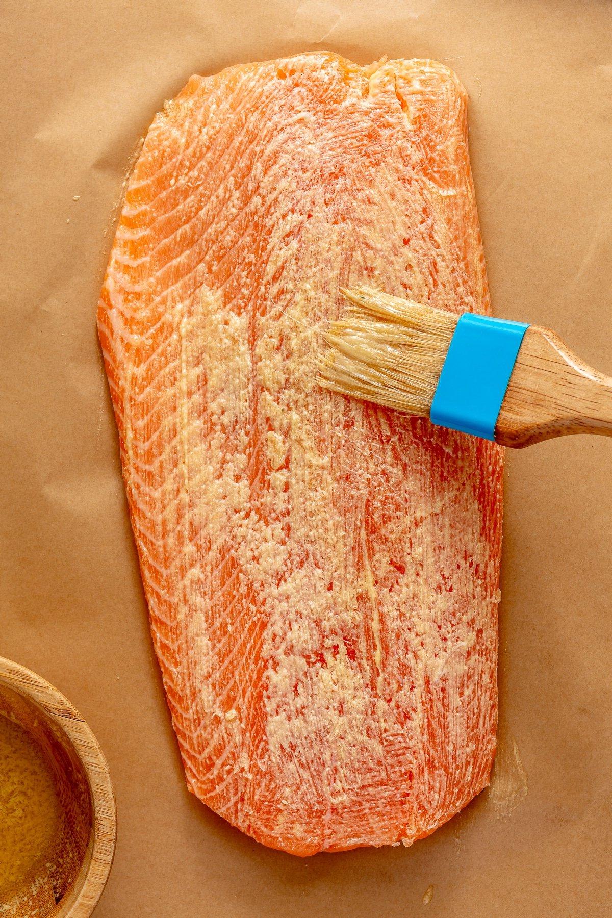 Lachsfilet auf Backpapier, die Oberseite wird mit Butter-Senf-Mischung bestrichen.