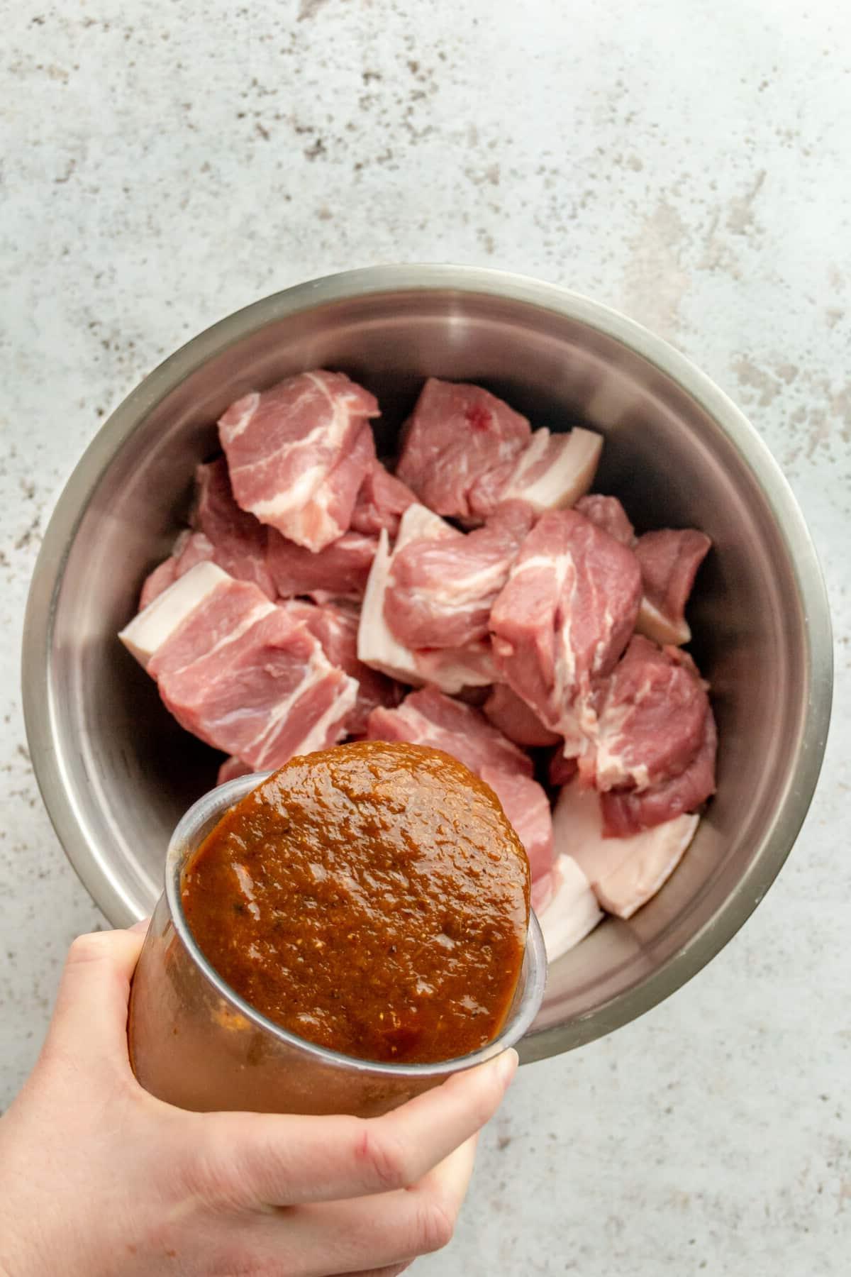 Die vorbereitete Marinade wird über die Schweineschulterstücke in einer großen Edelstahlschüssel auf hellem Hintergrund gegossen.