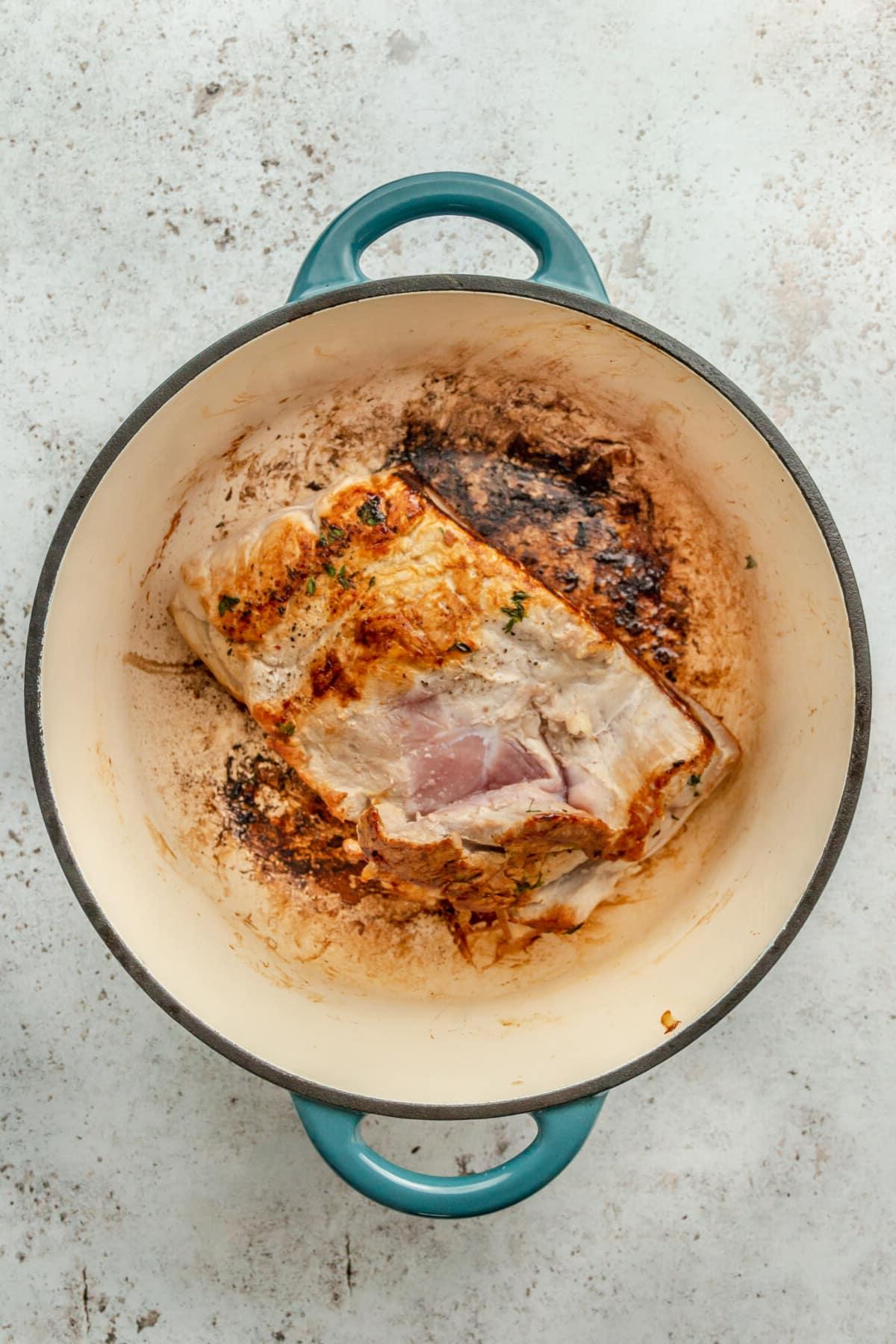 Ein angebratenes Schweinefilet liegt in einem Bräter auf einer hellgrauen Oberfläche.