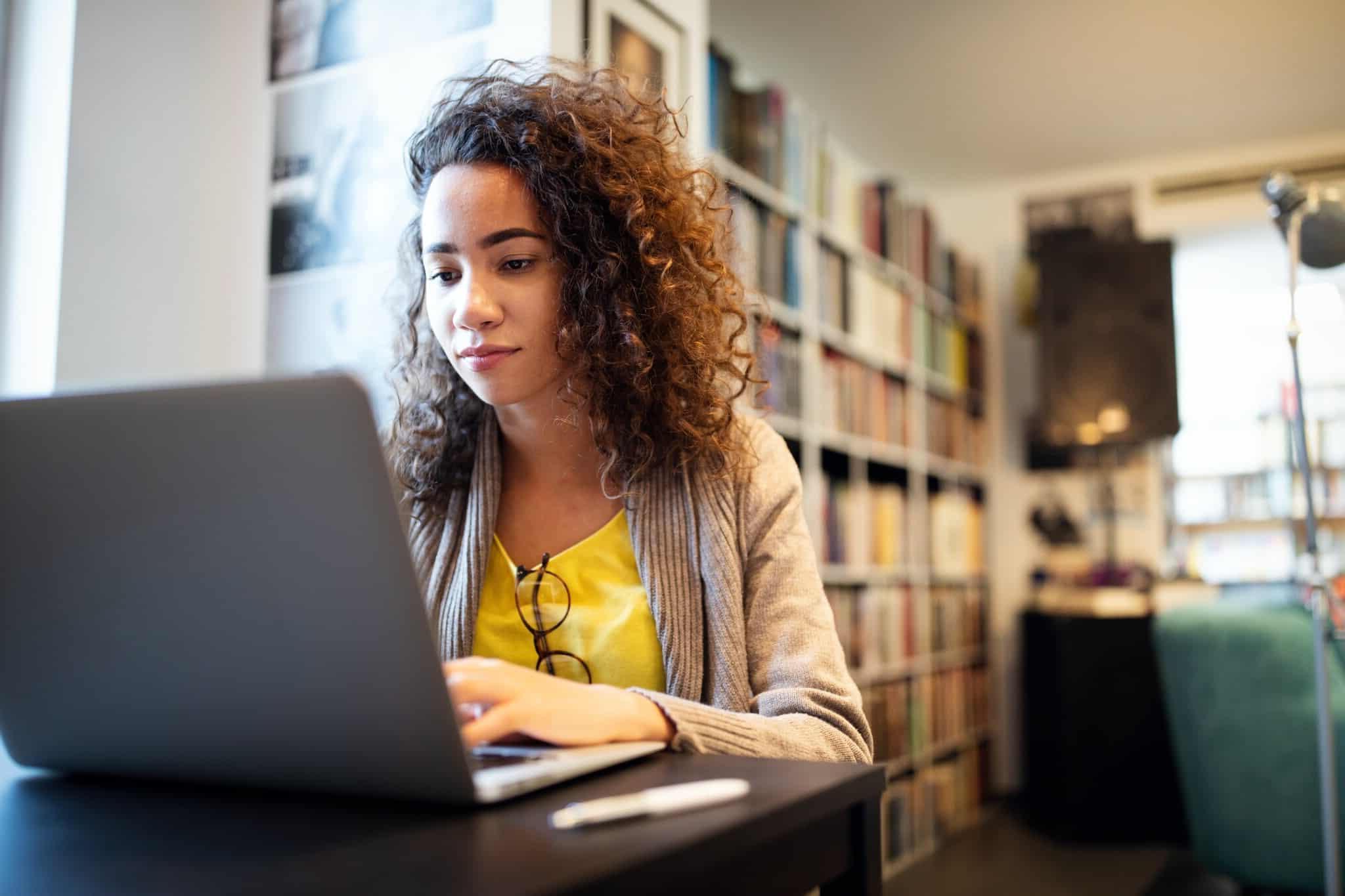 woman working at her laptop with bookshelves in the background