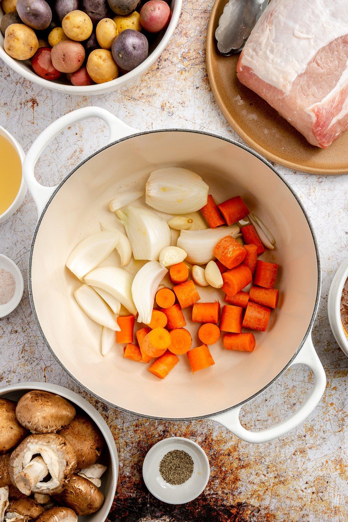 Stücke von leuchtend orangefarbenen Karotten und geschnittenen weißen Zwiebeln wurden in einen weißen, emaillierten Topf gelegt.
