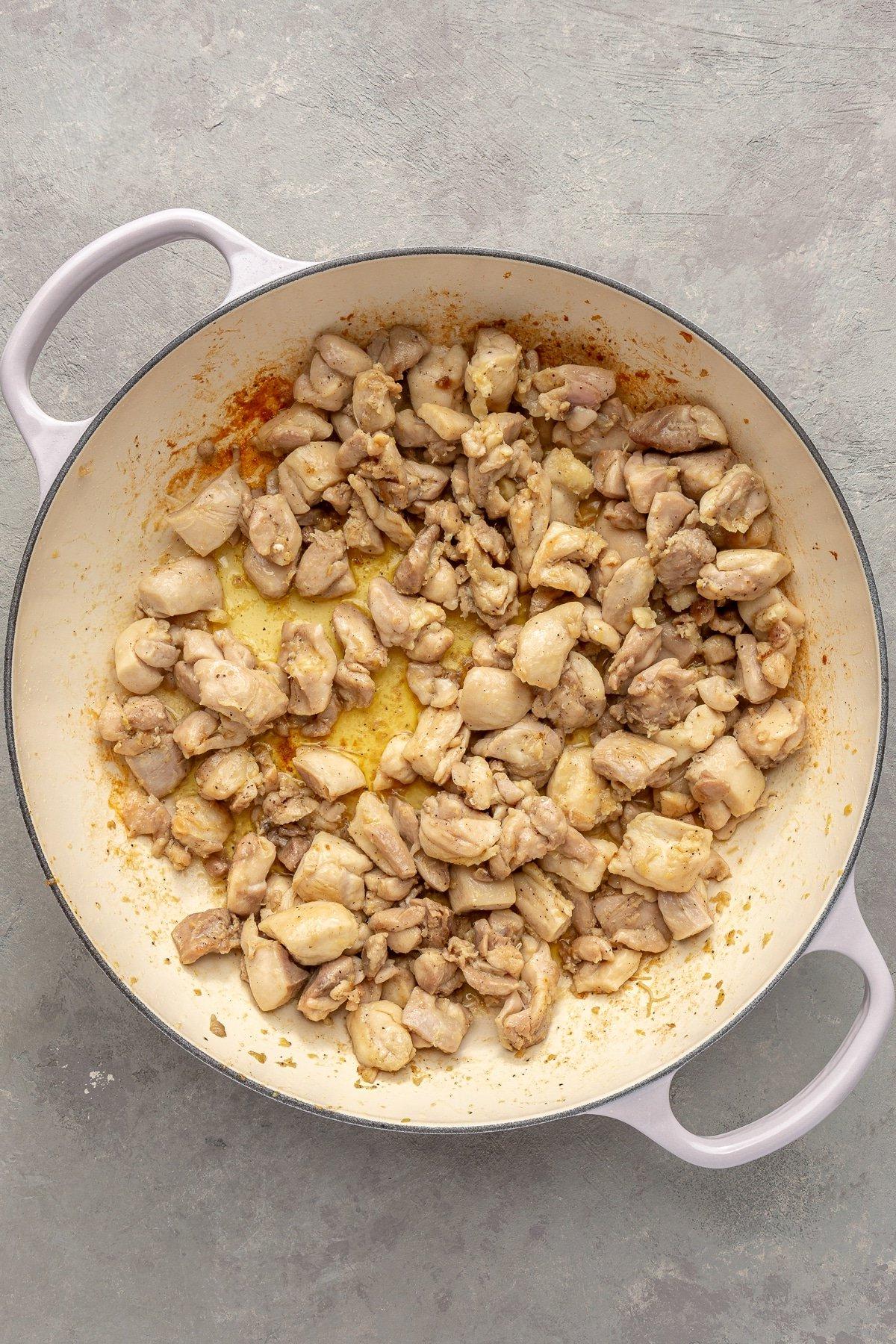 Einfaches Kürbiscurry-Rezept 5 Das Hähnchen wurde leicht angebraten und liegt in einem weißen emaillierten Topf mit verschiedenen Gewürzen.