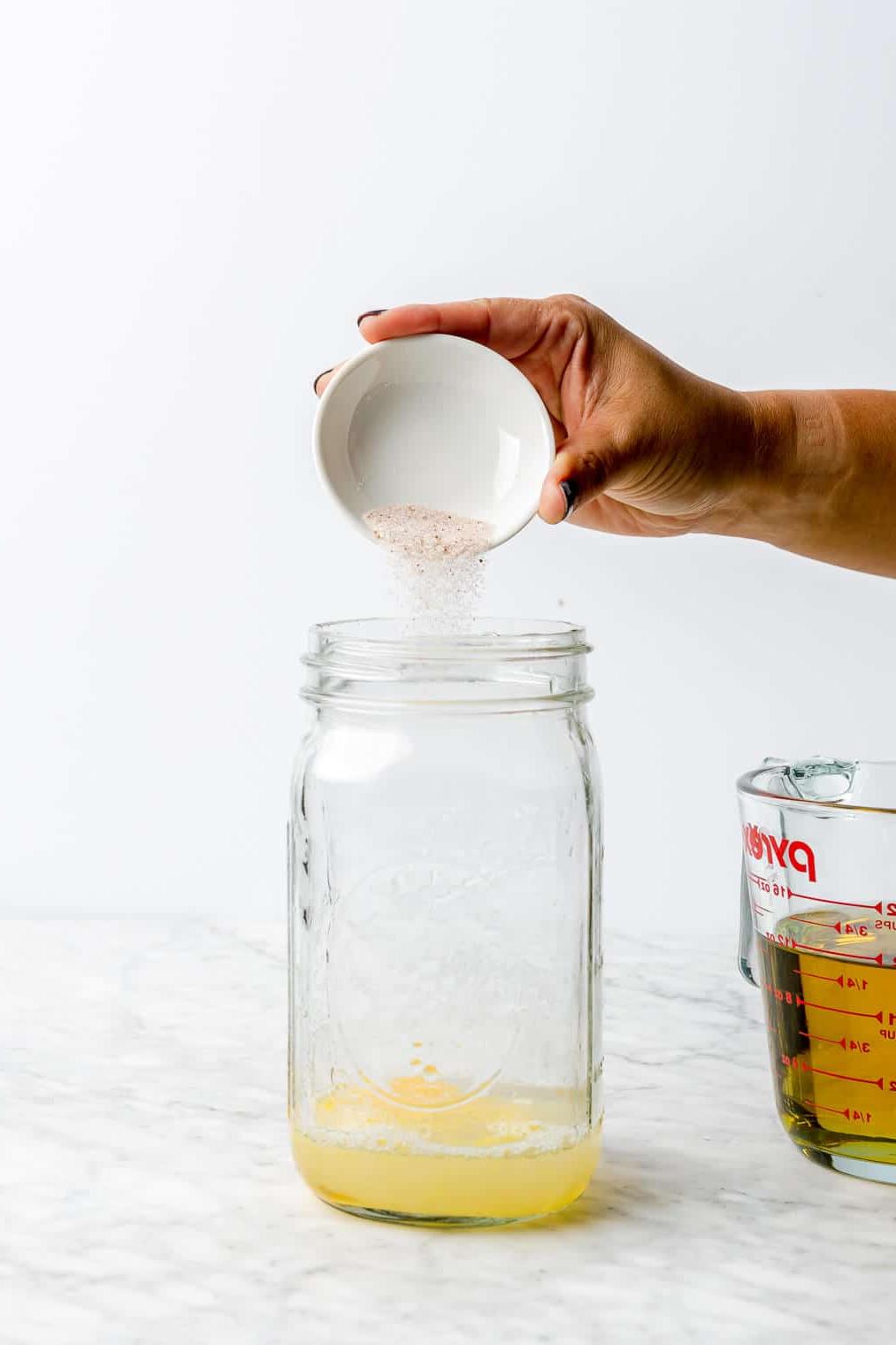 Hand, die Salz über einem aufgeschlagenen Ei und Zitronensaft in ein großes Einmachglas schüttet.