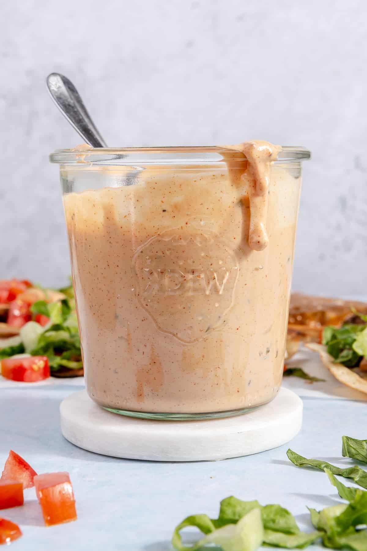 Ein Glas Burgersauce, umgeben von Toppings für Smash-Burger-Tacos.