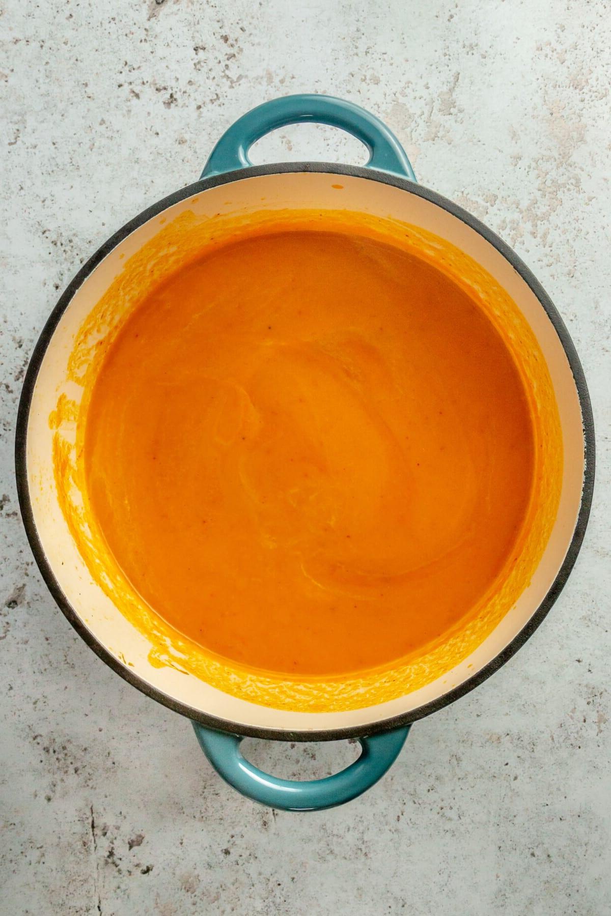 Pürierte, glatte Karottensuppe in einem blauen emaillierten Gusseisentopf.