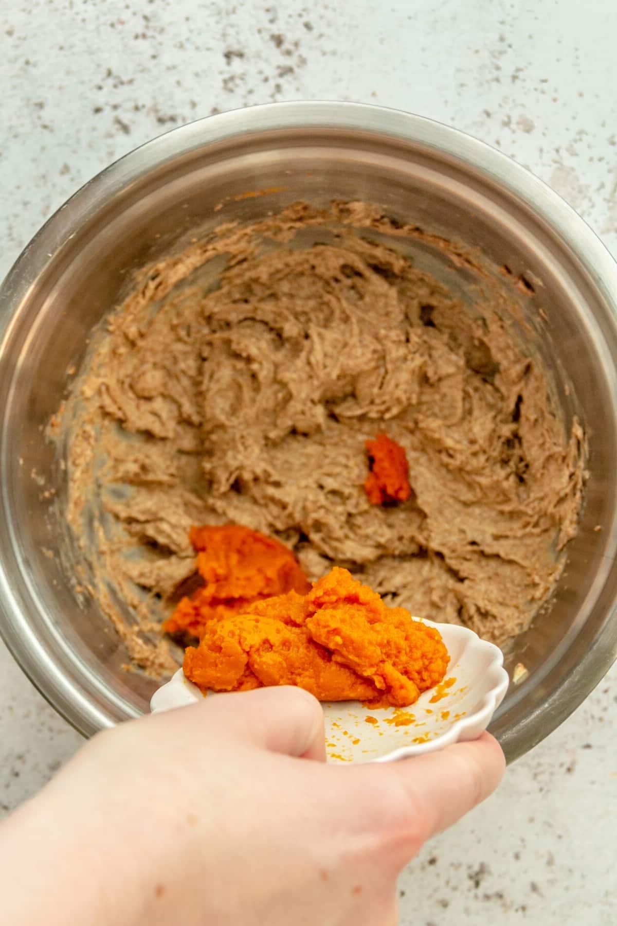 Kürbispüree wird in die geschlagene Butter-Zucker-Mischung in einer Edelstahlschüssel auf hellem Untergrund gegeben.
