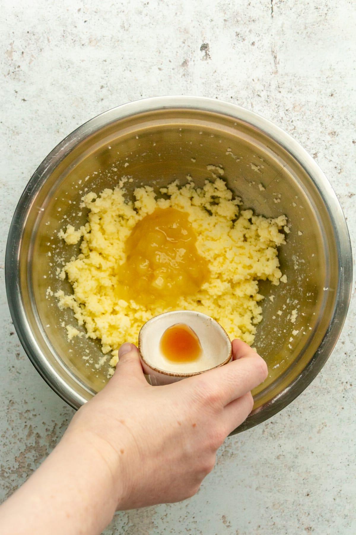 Vanilleextrakt wird über geschlagene Butter und Apfelmus in einer Edelstahlschüssel auf hellem grauem Untergrund gegeben.