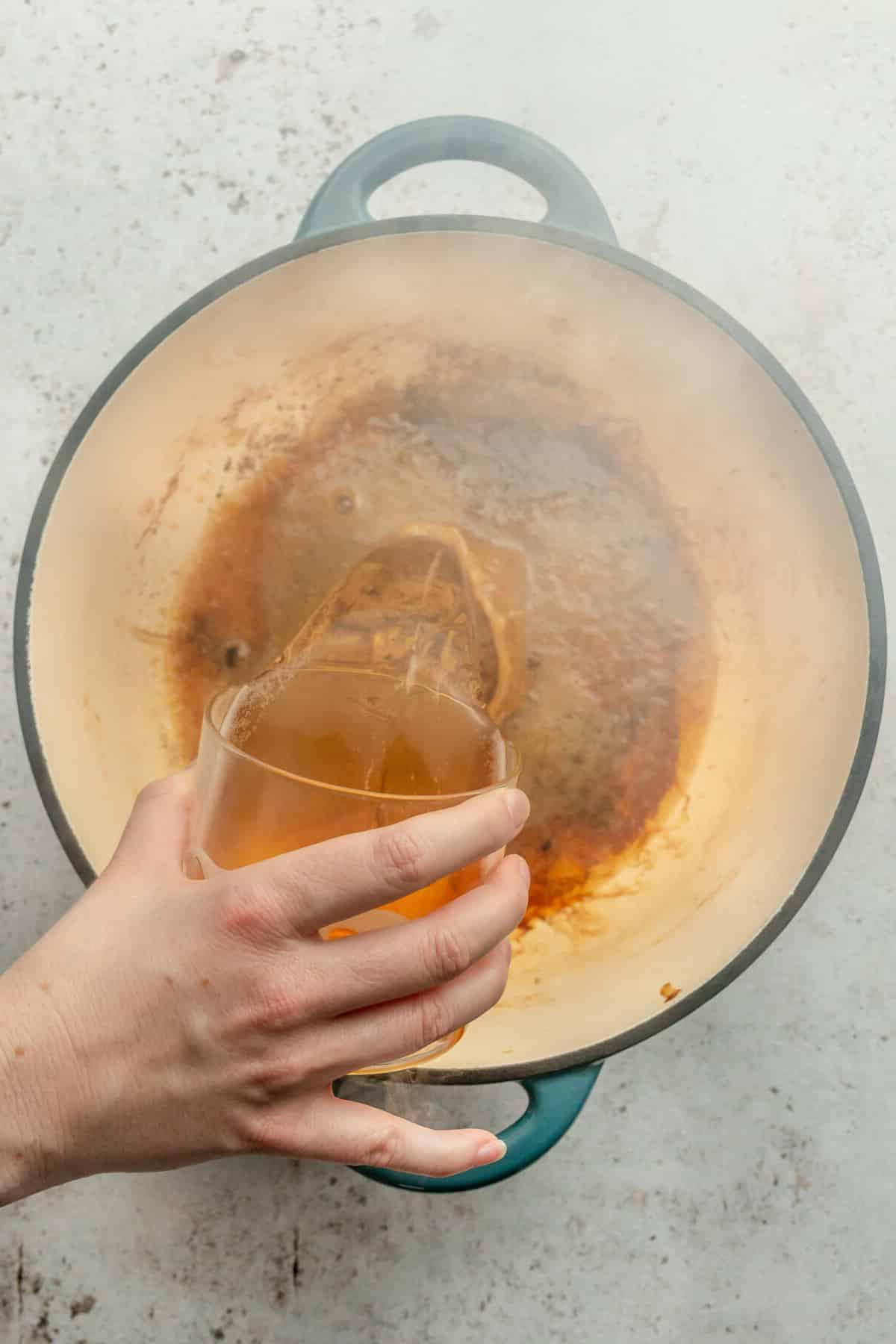 Apfelwein wird in einen heißen Bräter auf einer hellgrauen Oberfläche gegossen.
