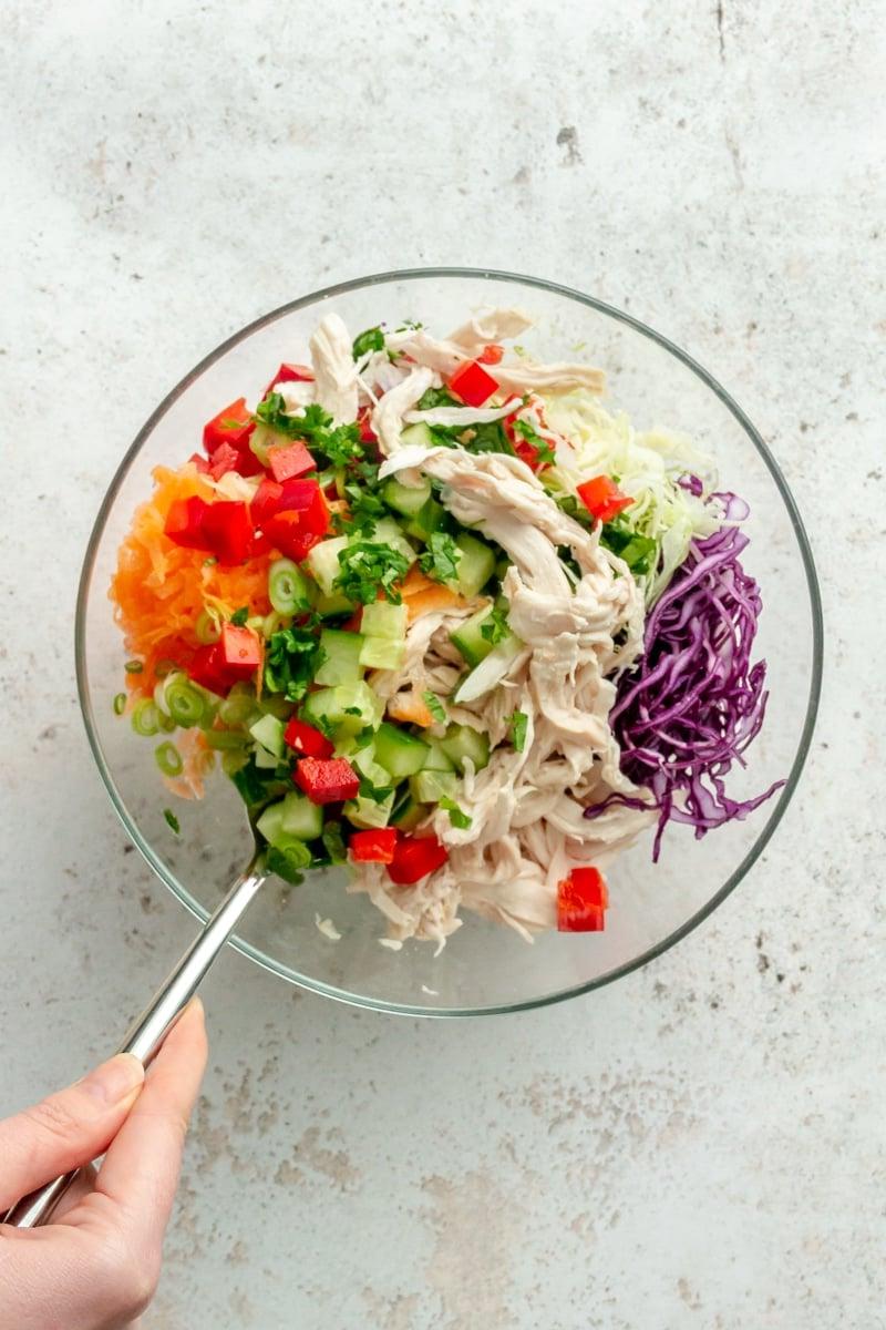 Zutaten für den Thai-inspirierten Hähnchensalat werden in einer Glasschüssel vermischt.