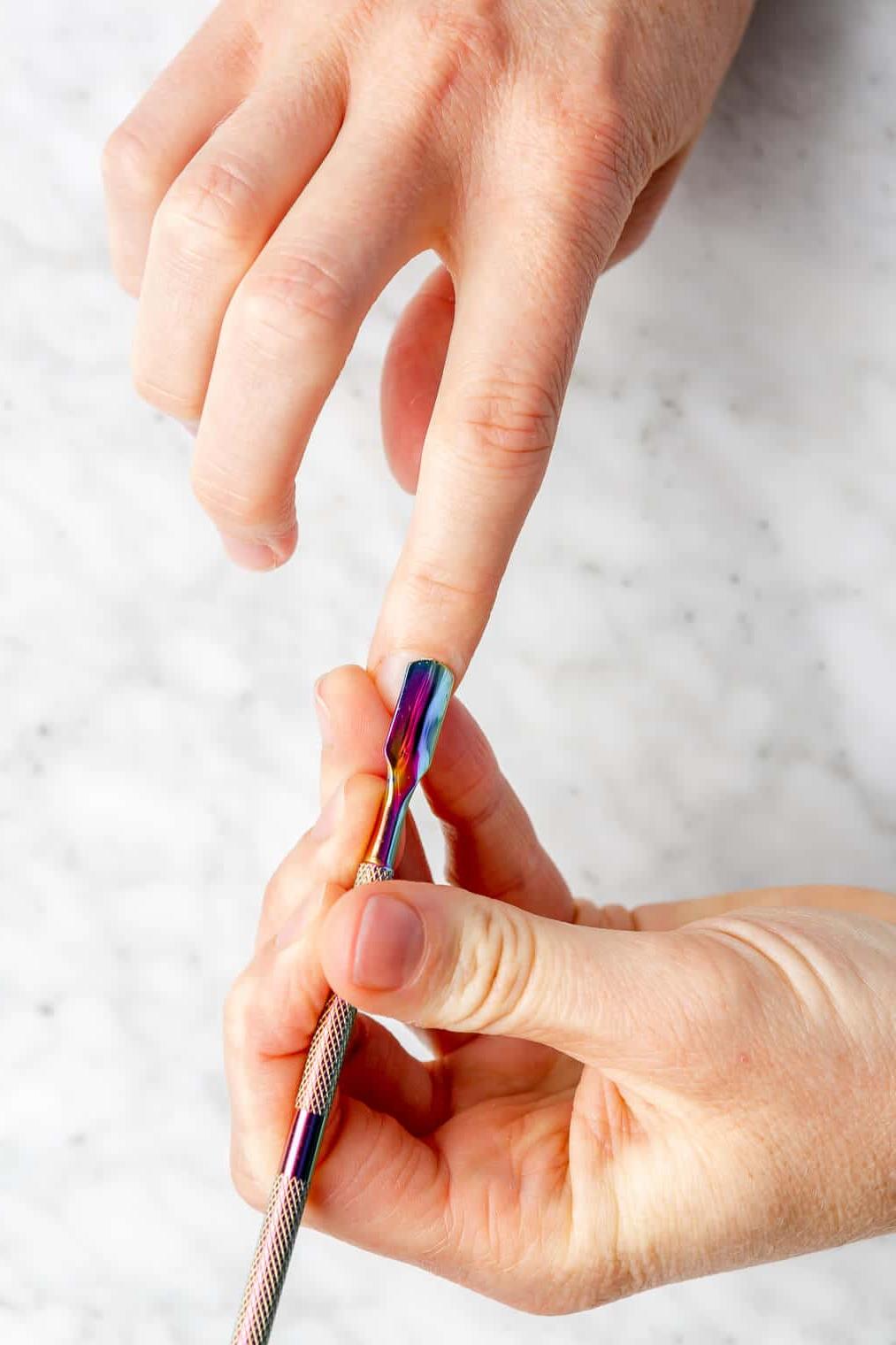 Hand hält Nagelhautwerkzeug, um Nagelhaut an der anderen Hand zurückzuschieben.