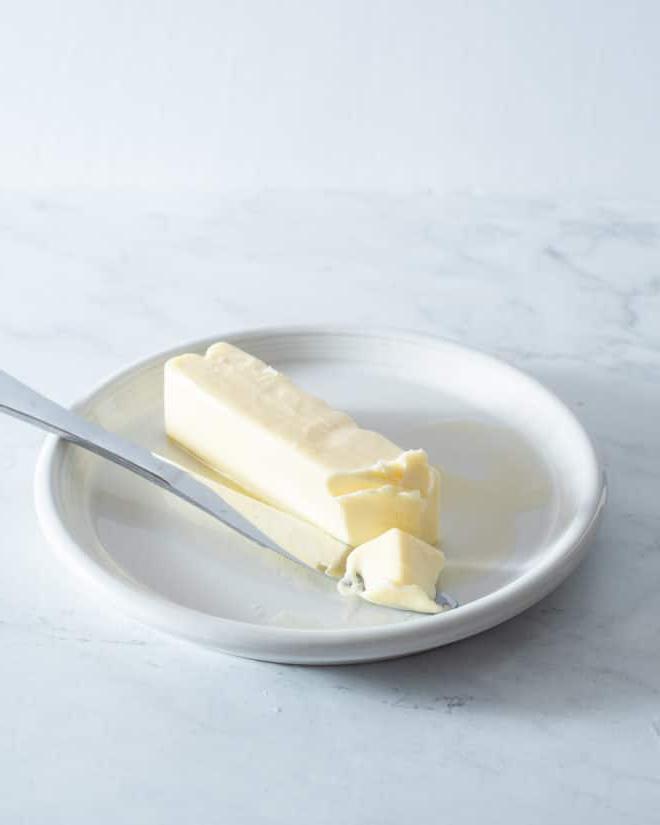 Ein Stück weiche Butter auf einem kleinen weißen Teller mit einem Buttermesser daneben