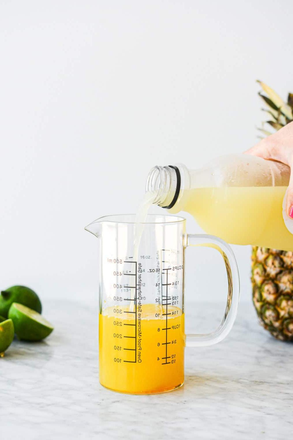 Eine Person gießt Limettensaft zusammen mit den anderen Ananas Margarita Zutaten in einen großen Messbecher aus Glas.
